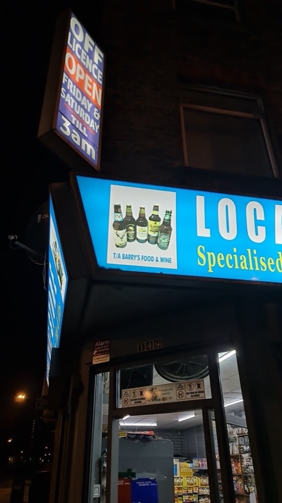 Barry's Food & Wine shopfront on Hoxton Street at night, blue off-licence sign lit up reading open till late